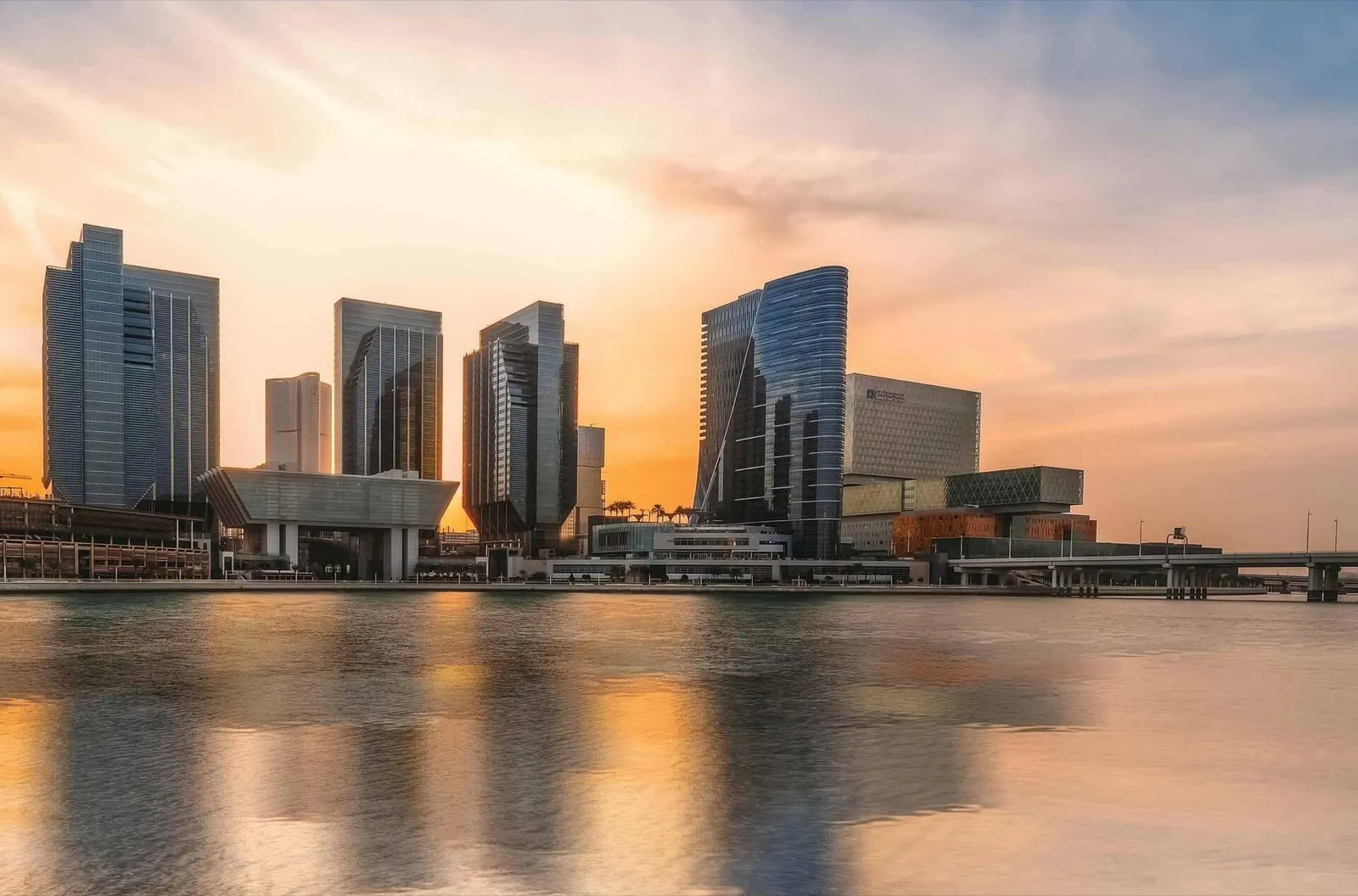 Office towers on Al Maryah Island reflected in the water at sunset