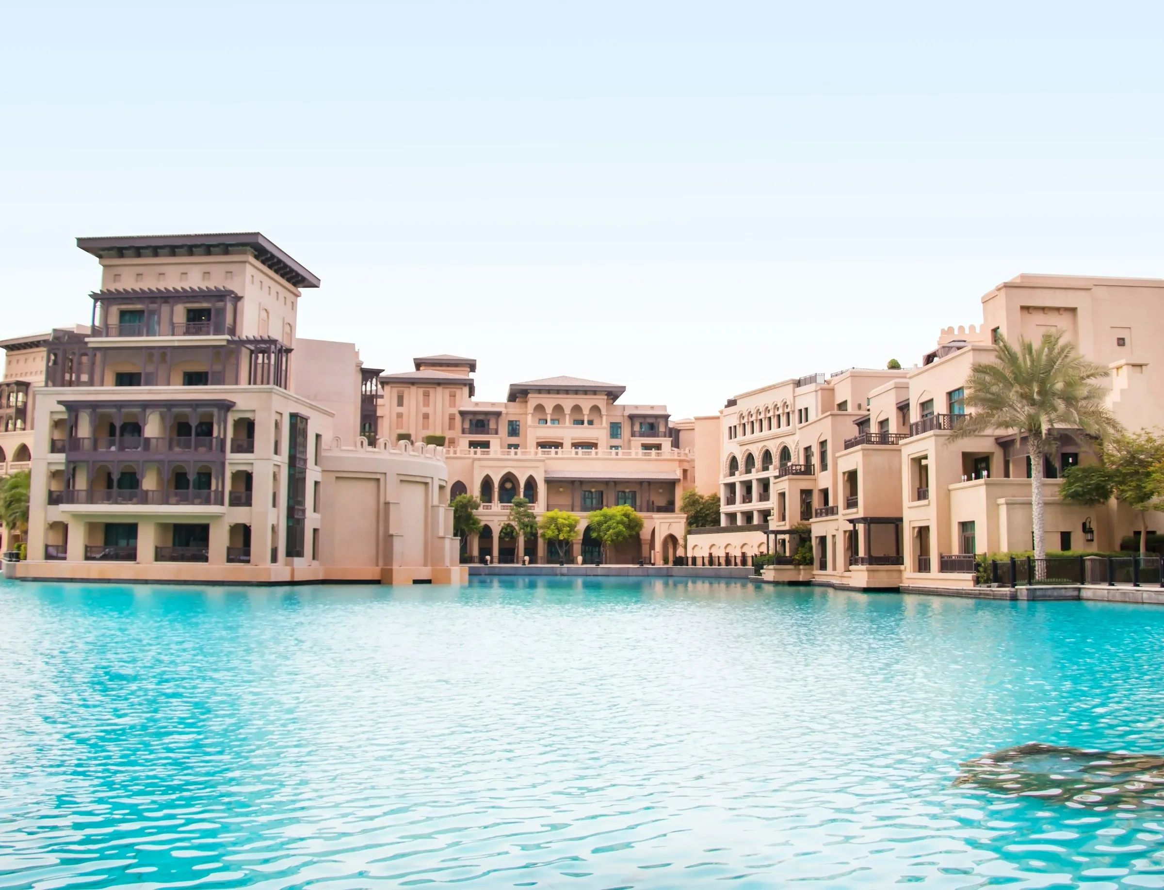 Arabian-style low-rise buildings with arched balconies beside a turquoise pool