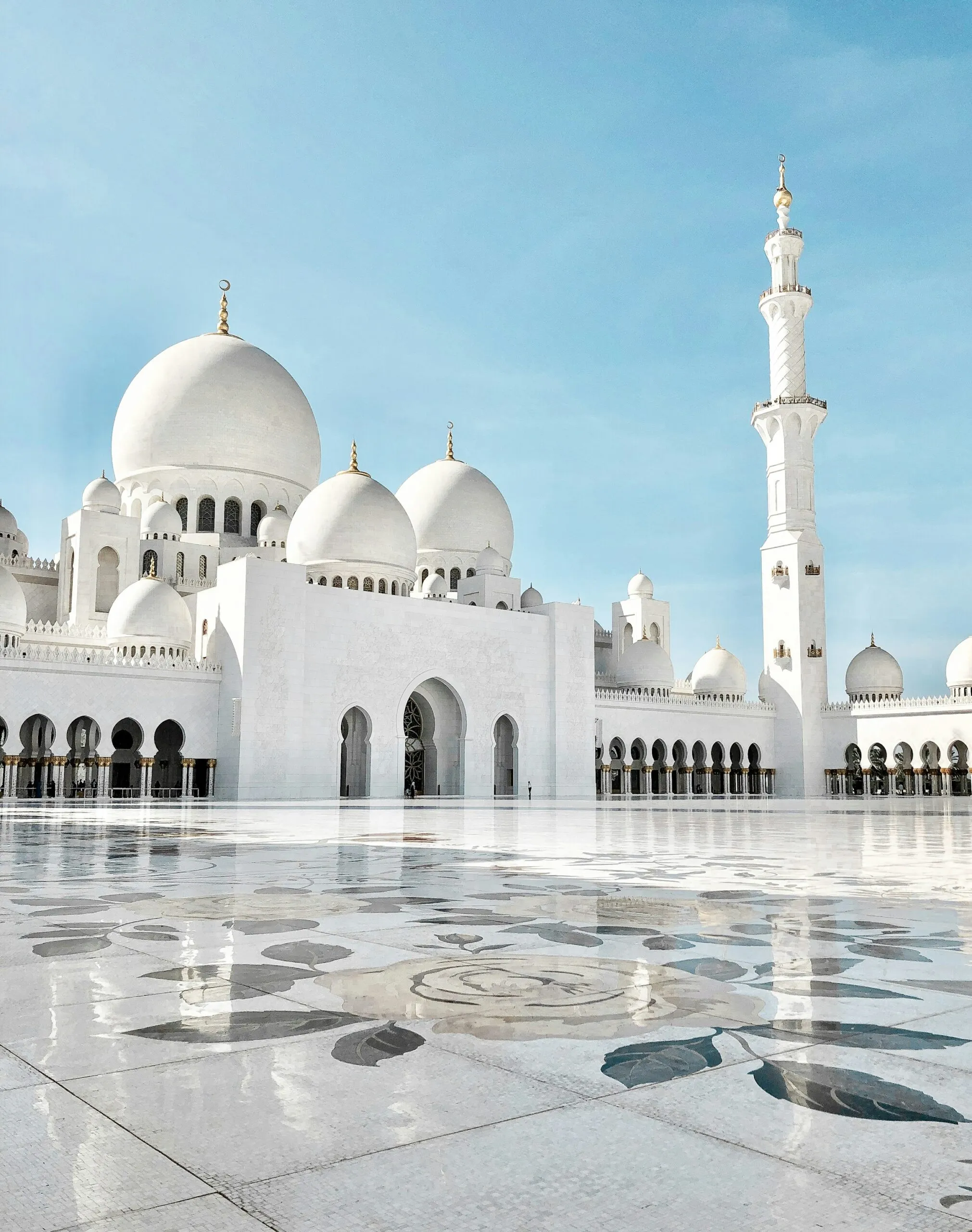 White domes and a minaret of the Sheikh Zayed Grand Mosque under a blue sky