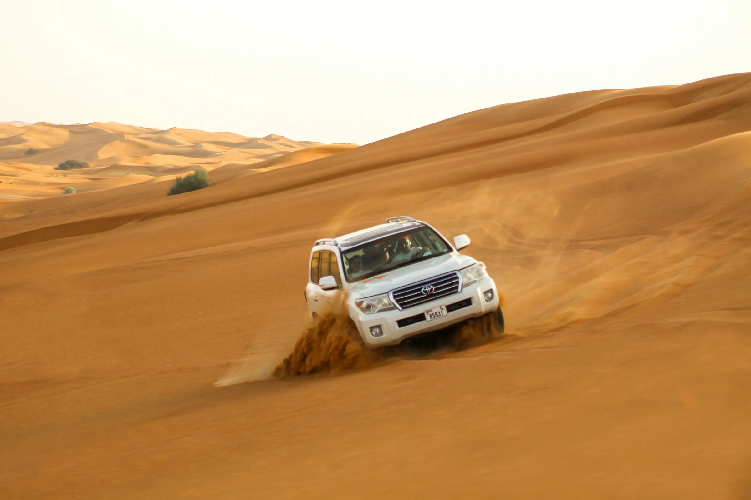 A white 4x4 driving over sand dunes in the desert